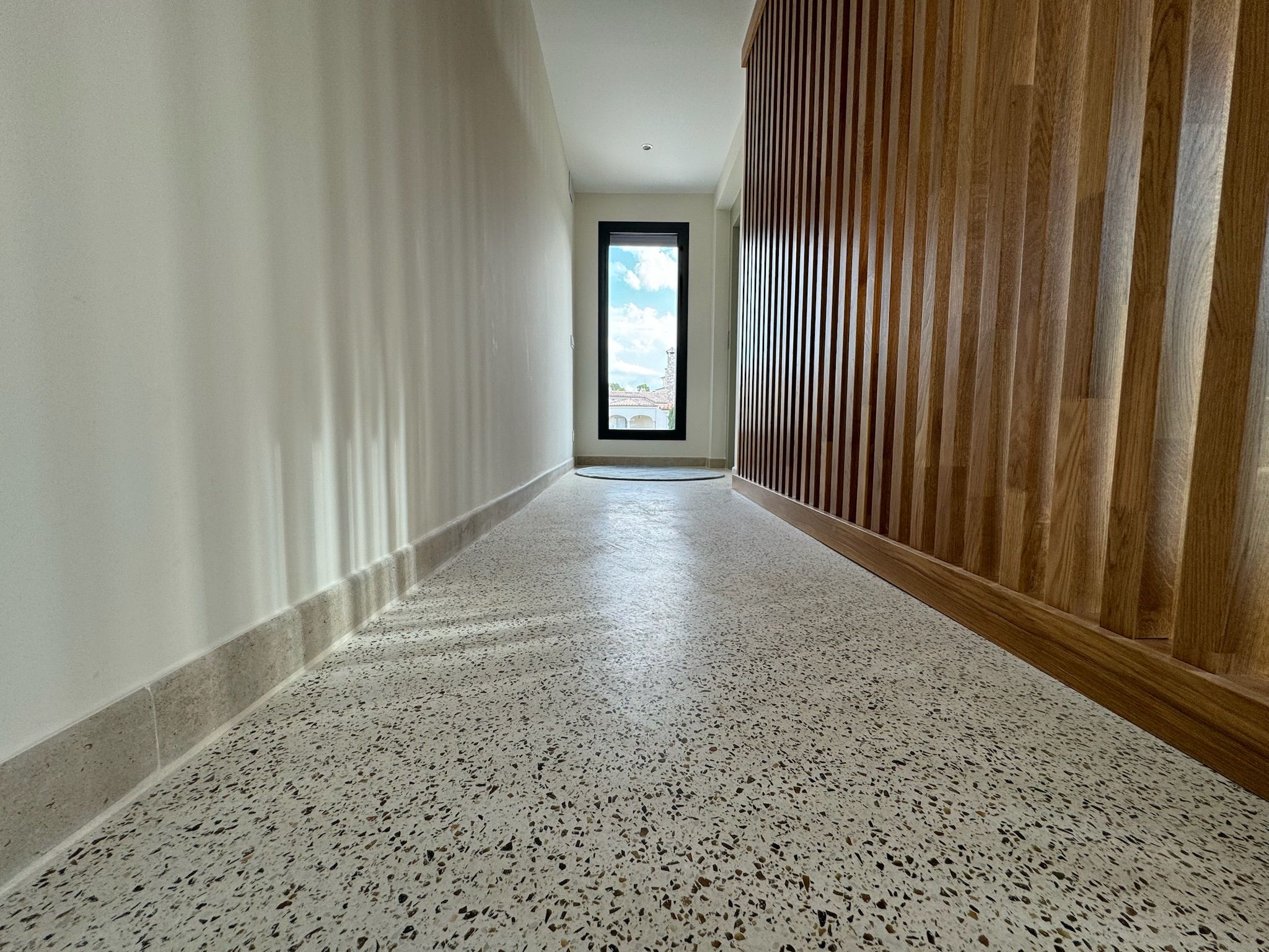 Pasillo residencial con Stone Feel granulado y lamas de madera en pared