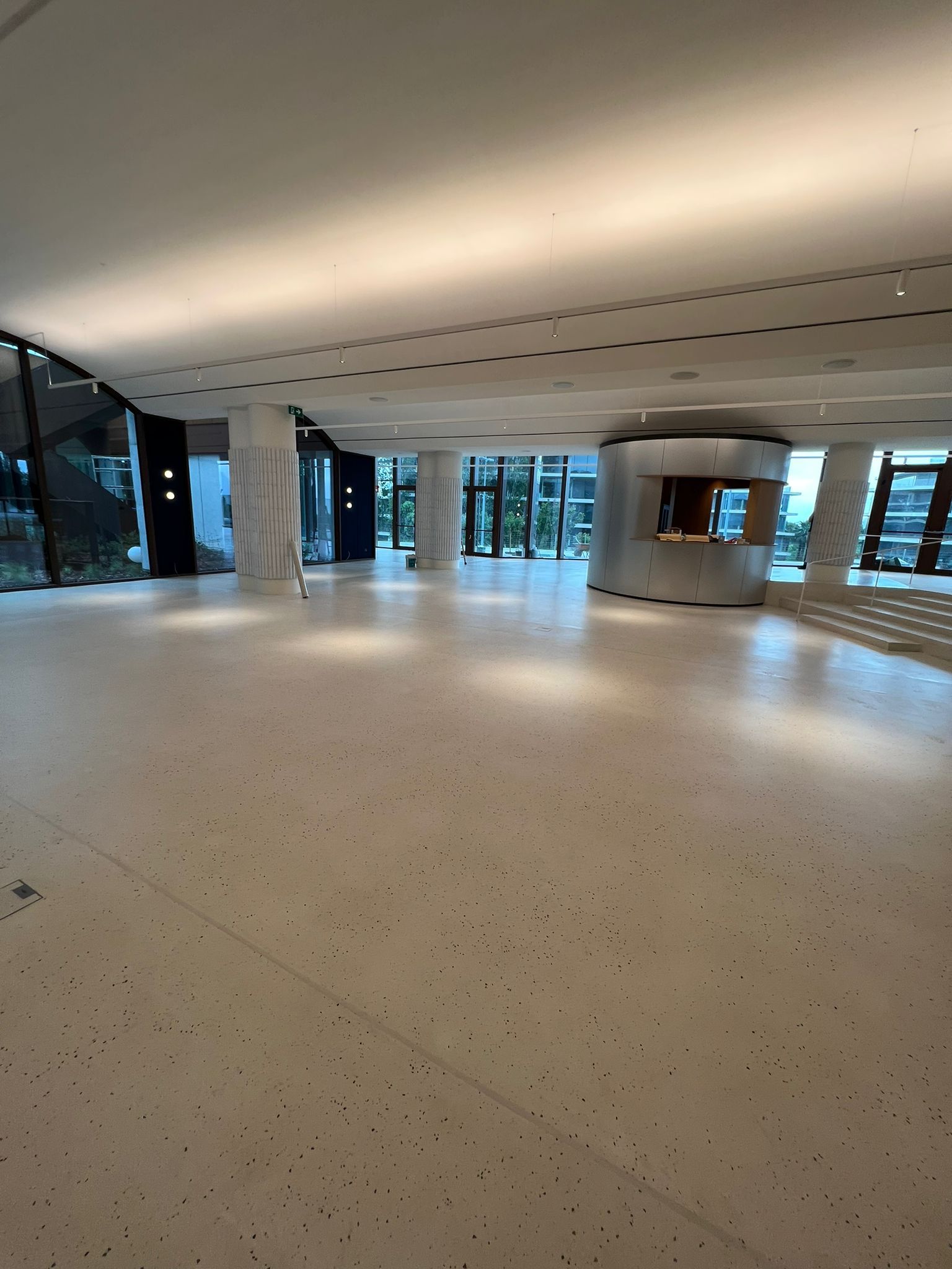 Lobby principal Grifols con suelo Stone Feel blanco, iluminación cenital y acceso curvo